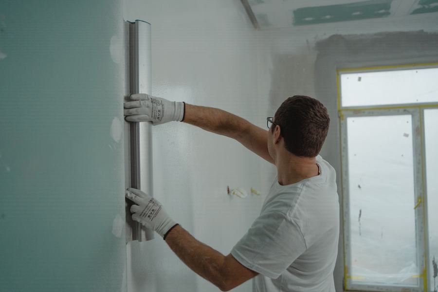 Homme en chemise blanche lissant un enduit sur un mur avec une grande lame métallique